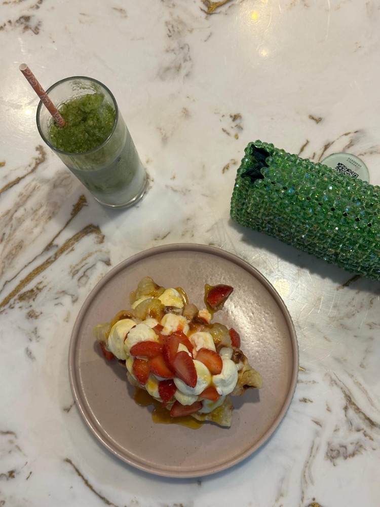 An emerald crystal-beaded clutch on a marble table with a green smoothie and dessert